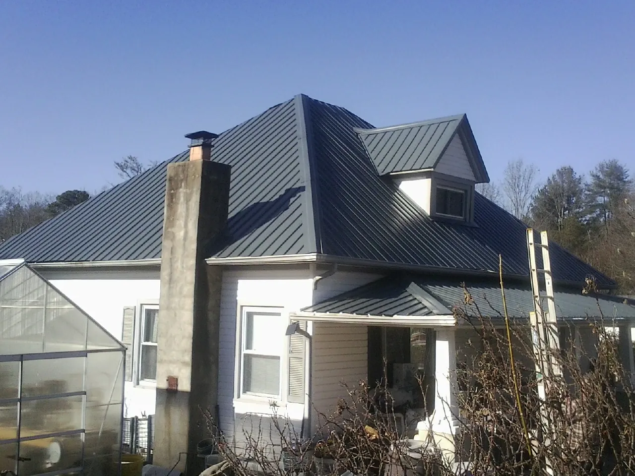 Dark blue standing seam metal roof on a white farmhouse with dormer — Slate & Tile Roof Repair by Roofing Brothers in Holly