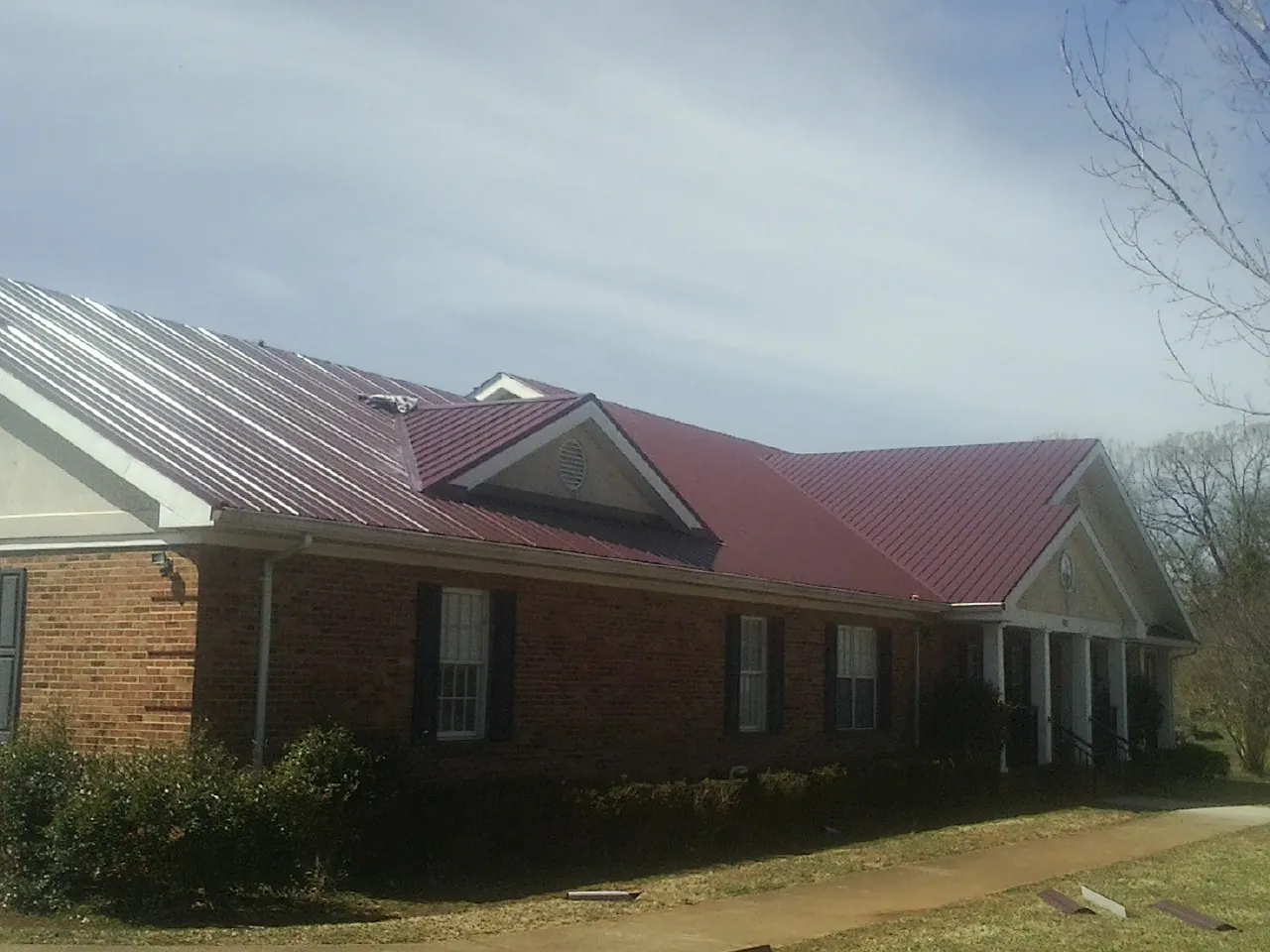 Red metal roof with gabled entries on a long brick building, from a Hail Damage Roof Repair job in Holly