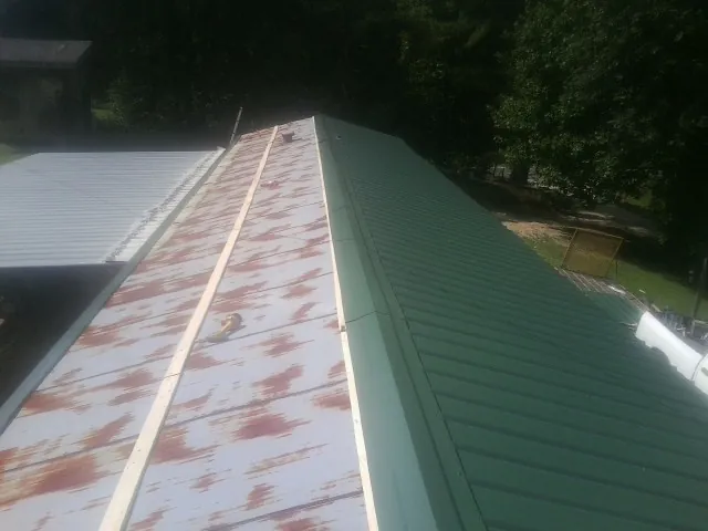 Old rusted panels beside newly installed green metal roofing — Wind Damage Roof Repair by Roofing Brothers in Holly