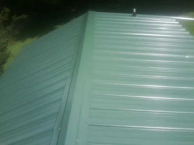 New green metal panels meeting at the ridge of a roof — Flat Roof Repair work by our crew in Holly