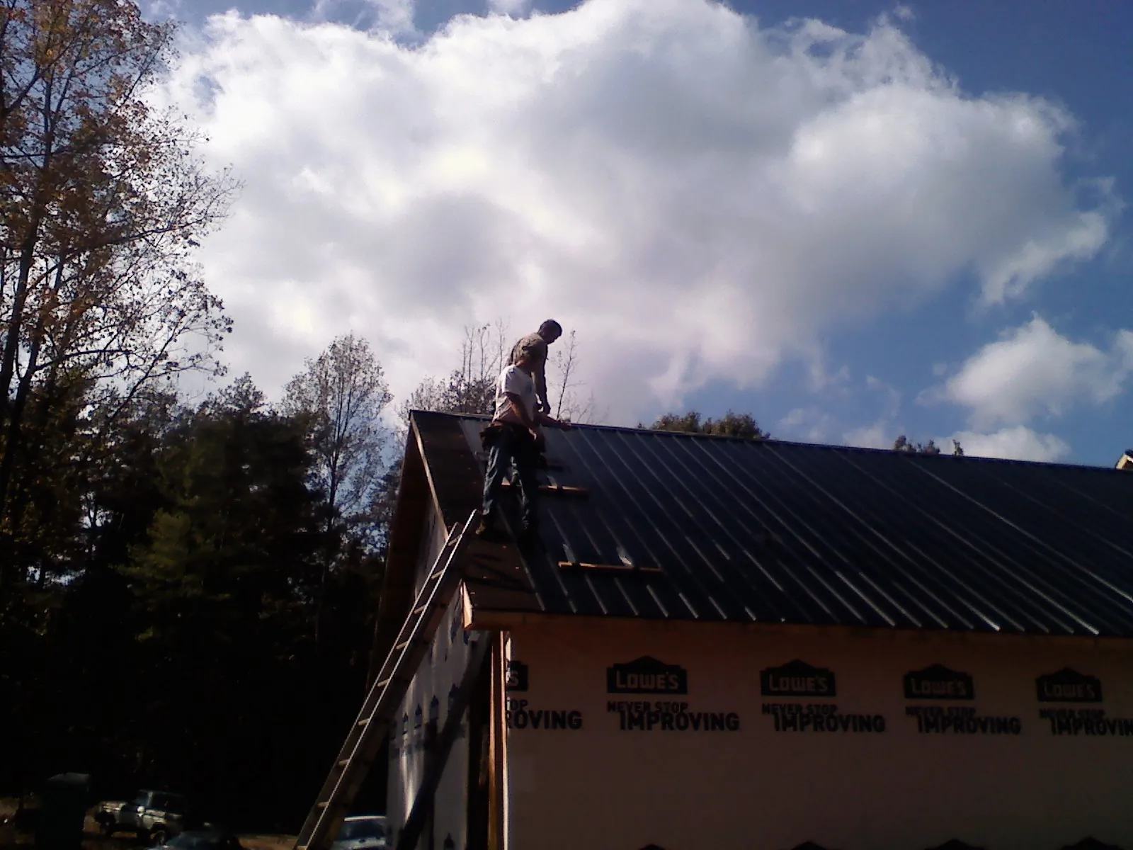 Roofer fastening dark metal panels high against a cloudy sky, from a Roof Inspection job in Holly