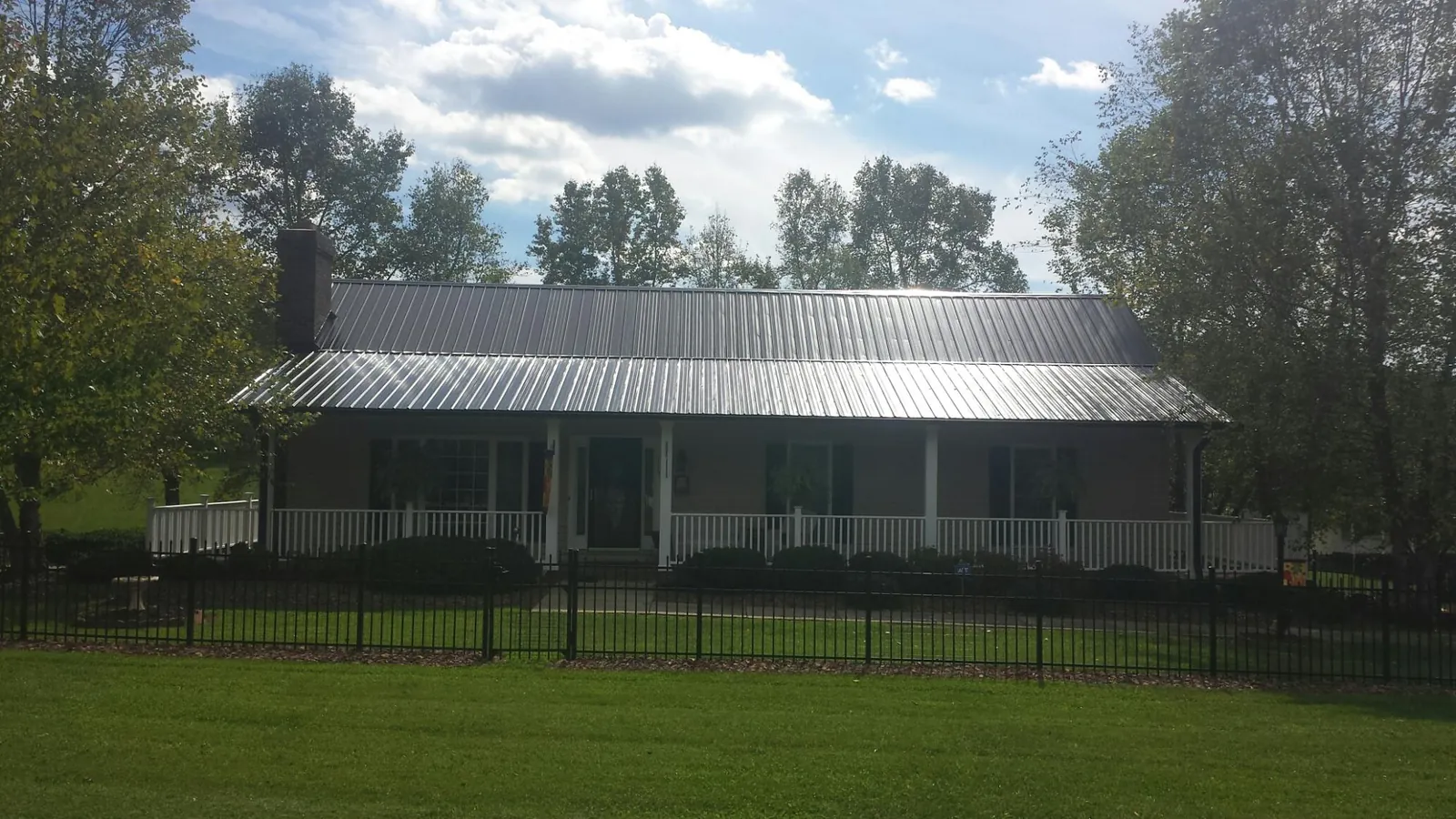 Gray metal roof on a brick ranch with a full width front porch — Gutter Guard Installation work by our crew in Holly