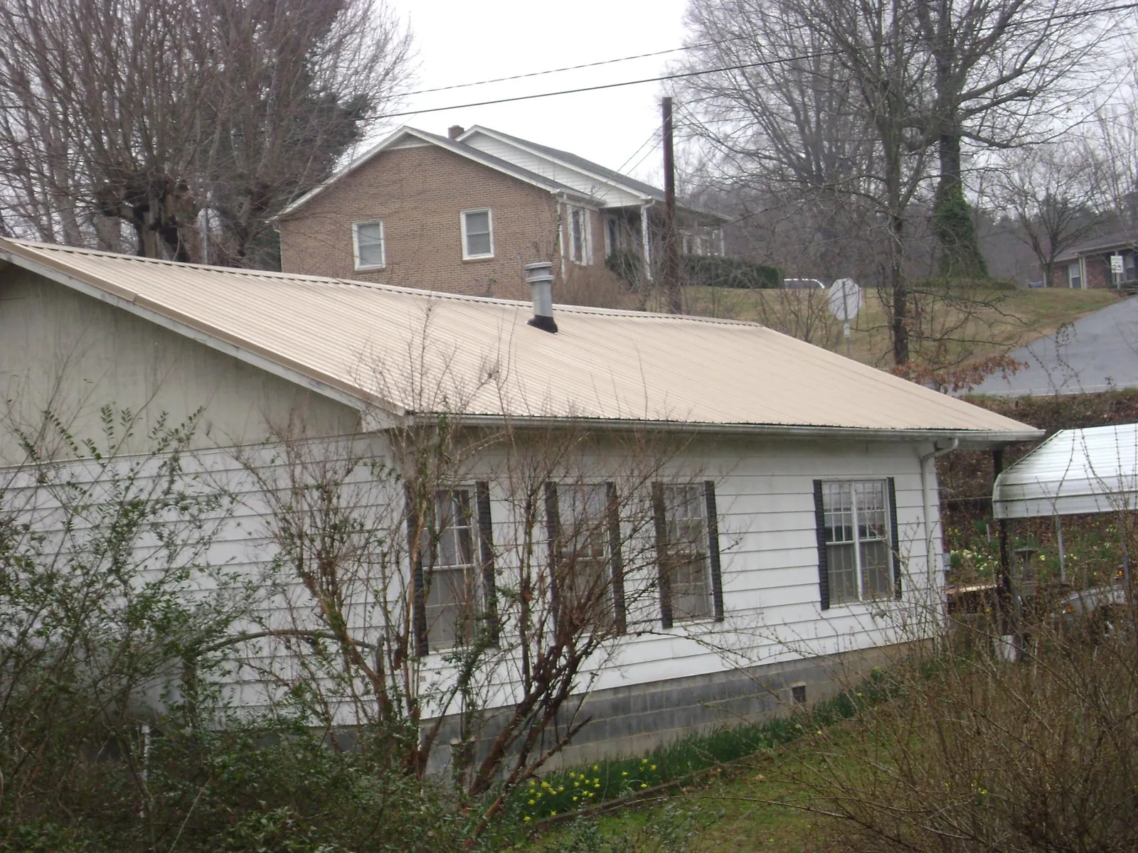 Tan metal roof on a white sided house set into a hillside — Commercial Roofing by Roofing Brothers in Holly