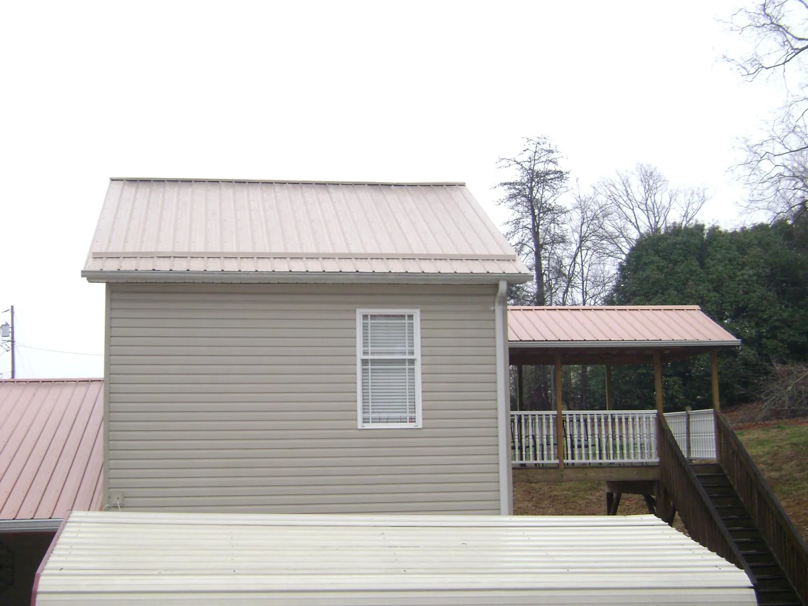 Tan metal roofs on a two story addition and attached porch, from a Roof Replacement job in Holly