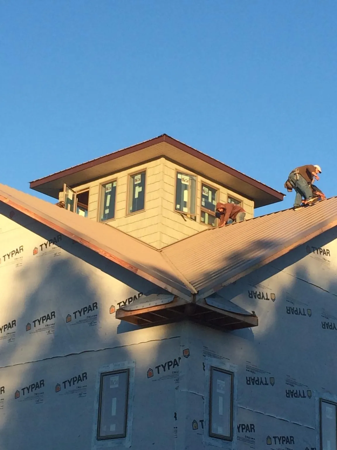 Roofers working around a rooftop cupola on a new metal roof at sunset — Roof Waterproofing in Holly by Roofing Brothers